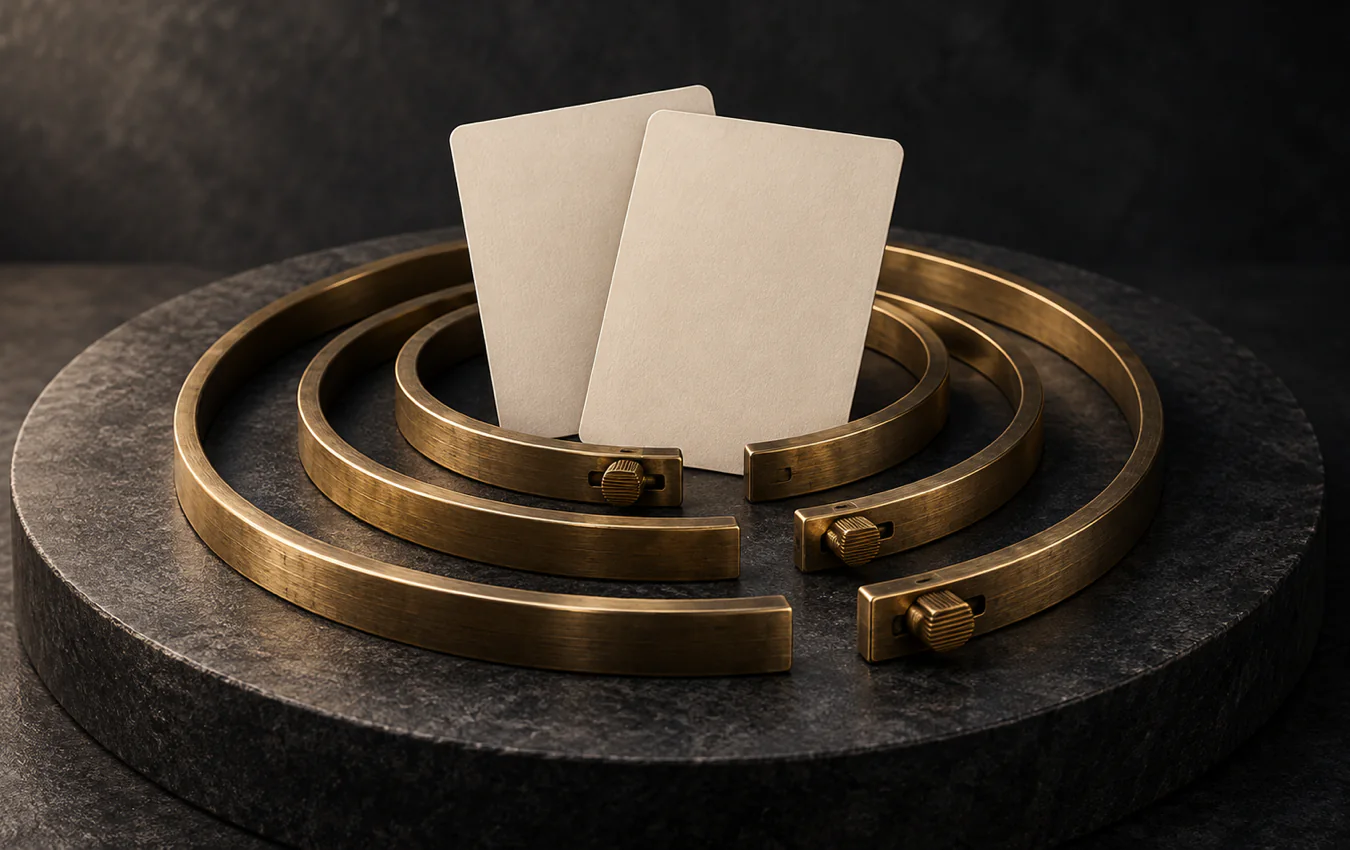 Two blank ivory playing cards rest inside adjustable nested brass rings on a dark stone platform
